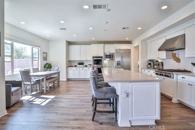 kitchen featuring visible vents, wall chimney range hood, and built in appliances