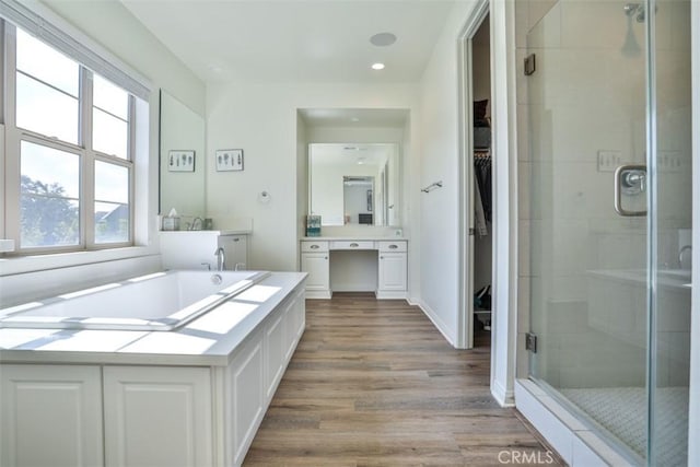 full bathroom featuring vanity, a walk in closet, a shower stall, a garden tub, and wood finished floors