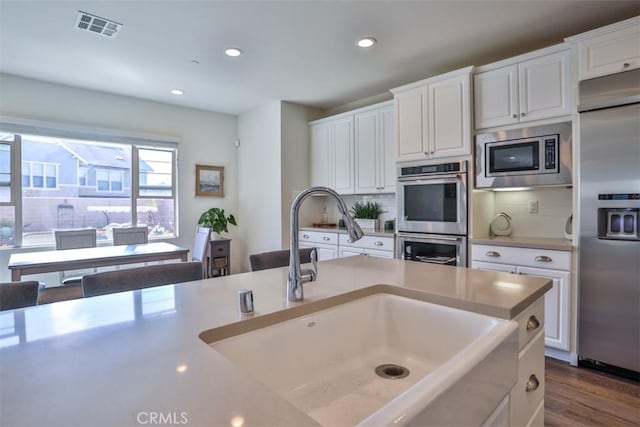kitchen with built in appliances, visible vents, backsplash, and a sink