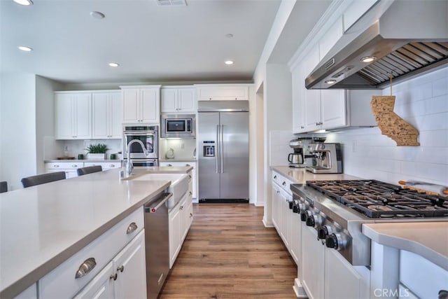 kitchen with white cabinetry, wall chimney range hood, built in appliances, and light countertops