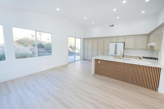 kitchen with light wood-style flooring, freestanding refrigerator, a peninsula, light countertops, and a sink