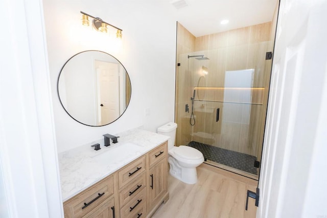 bathroom featuring wood finished floors, a stall shower, vanity, and toilet