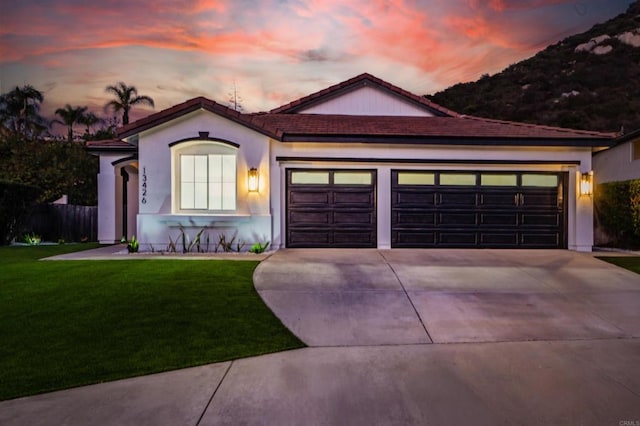 view of front facade with stucco siding, a lawn, a garage, driveway, and a tiled roof