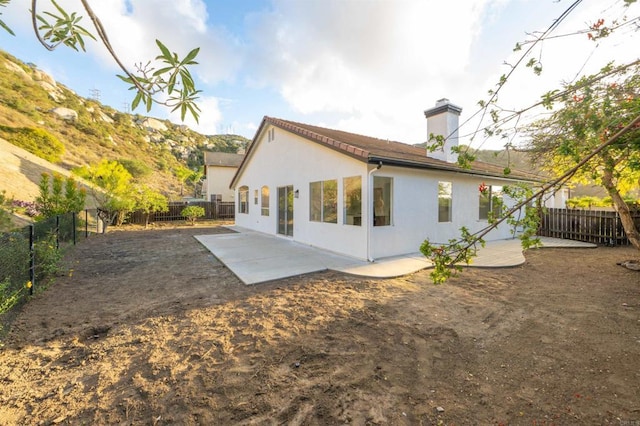 rear view of property with a fenced backyard, a patio, a chimney, and stucco siding