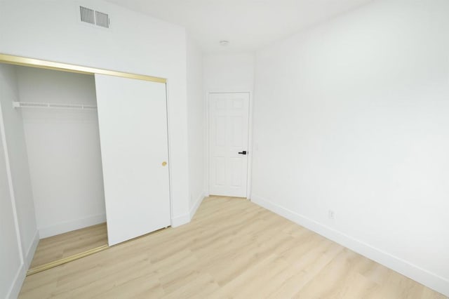 unfurnished bedroom featuring baseboards, a closet, visible vents, and wood finished floors