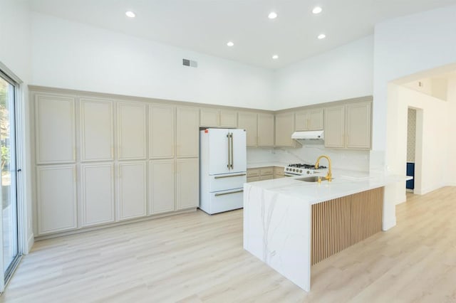 kitchen featuring white appliances, visible vents, a towering ceiling, a peninsula, and under cabinet range hood