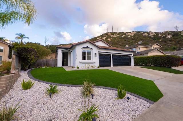 mediterranean / spanish-style home featuring driveway, an attached garage, fence, a front lawn, and stucco siding