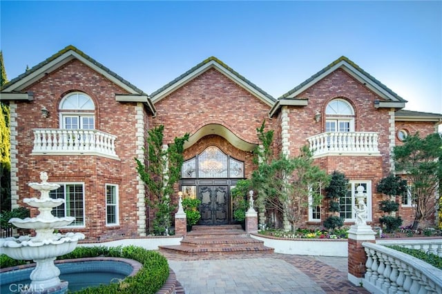 view of front of house featuring french doors, a balcony, and brick siding