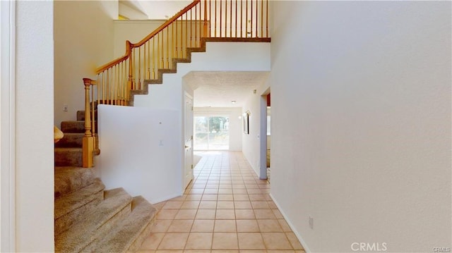 corridor with stairway, a towering ceiling, baseboards, and light tile patterned floors