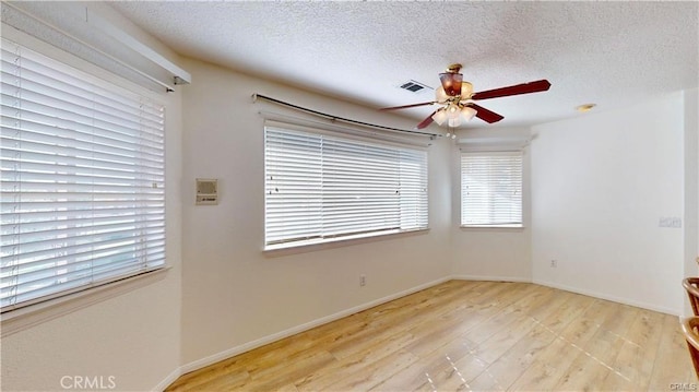 empty room featuring a textured ceiling, ceiling fan, visible vents, baseboards, and light wood-type flooring