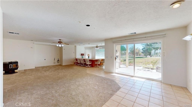 unfurnished living room featuring a textured ceiling, a wood stove, visible vents, and a ceiling fan