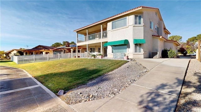 view of front of property with stucco siding, fence, a balcony, a tiled roof, and a front lawn