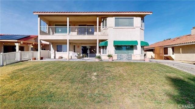 back of house with a balcony, a yard, fence, and stucco siding