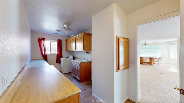 kitchen featuring light countertops, a sink, a textured ceiling, ceiling fan, and washer and dryer