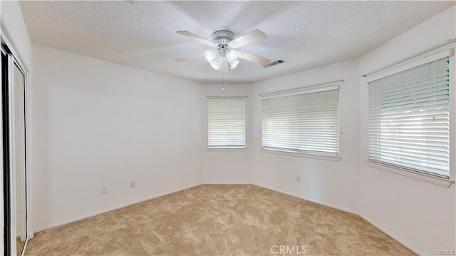 empty room with ceiling fan, visible vents, a textured ceiling, and light colored carpet