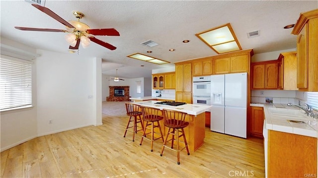 kitchen with white appliances, visible vents, a kitchen island, a kitchen bar, and a sink