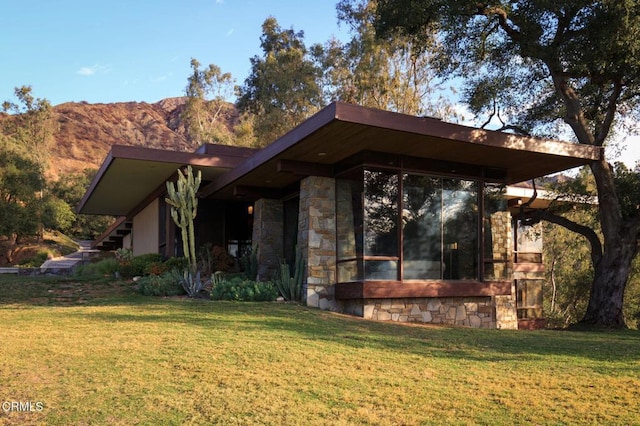 view of property exterior featuring a yard, stone siding, and a mountain view