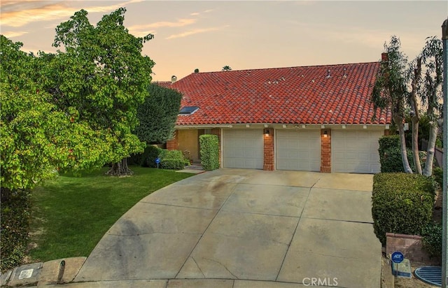 mediterranean / spanish house with an attached garage, brick siding, concrete driveway, a tiled roof, and a yard