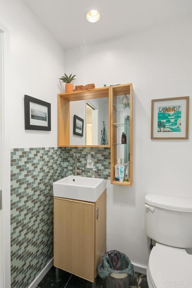 half bathroom with toilet, wainscoting, tile walls, and vanity