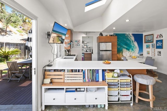 interior space with freestanding refrigerator, white cabinetry, a sink, vaulted ceiling with skylight, and concrete floors