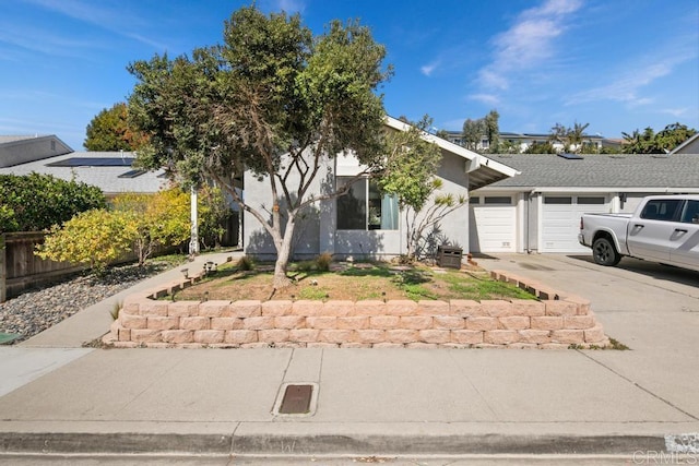 view of property hidden behind natural elements featuring an attached garage, fence, concrete driveway, and stucco siding