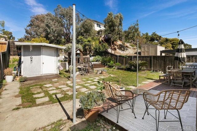 view of yard featuring a storage shed, a fenced backyard, a deck, and an outbuilding