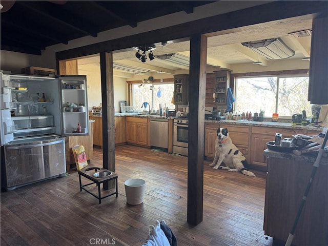 kitchen with brown cabinetry, appliances with stainless steel finishes, dark wood-type flooring, and beam ceiling