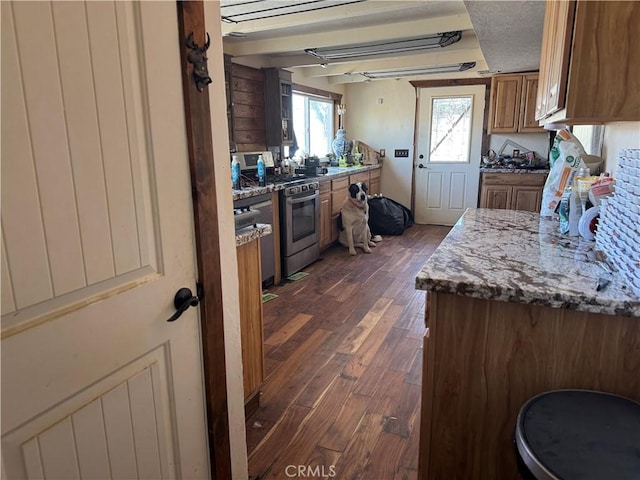 kitchen featuring stainless steel gas stove, stone counters, brown cabinetry, and dark wood-style flooring