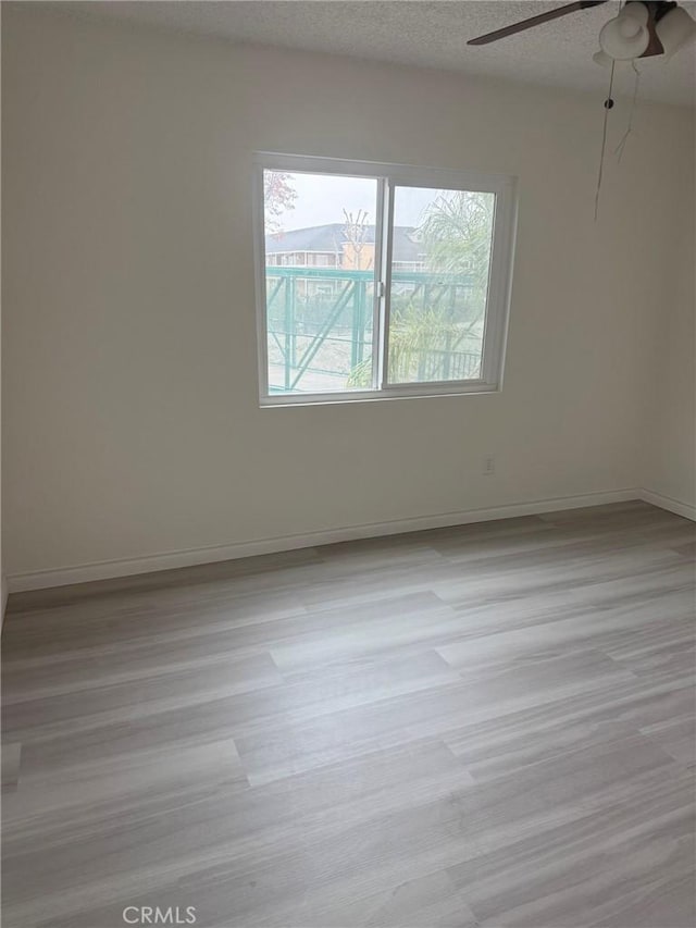 unfurnished room with ceiling fan, a textured ceiling, baseboards, and wood finished floors