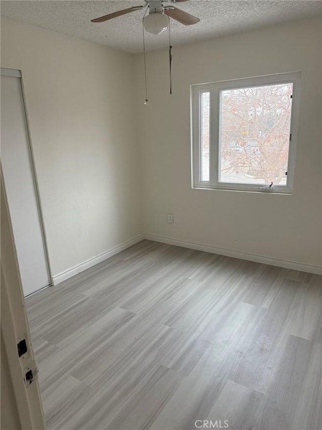 spare room featuring a textured ceiling, light wood finished floors, a ceiling fan, and baseboards