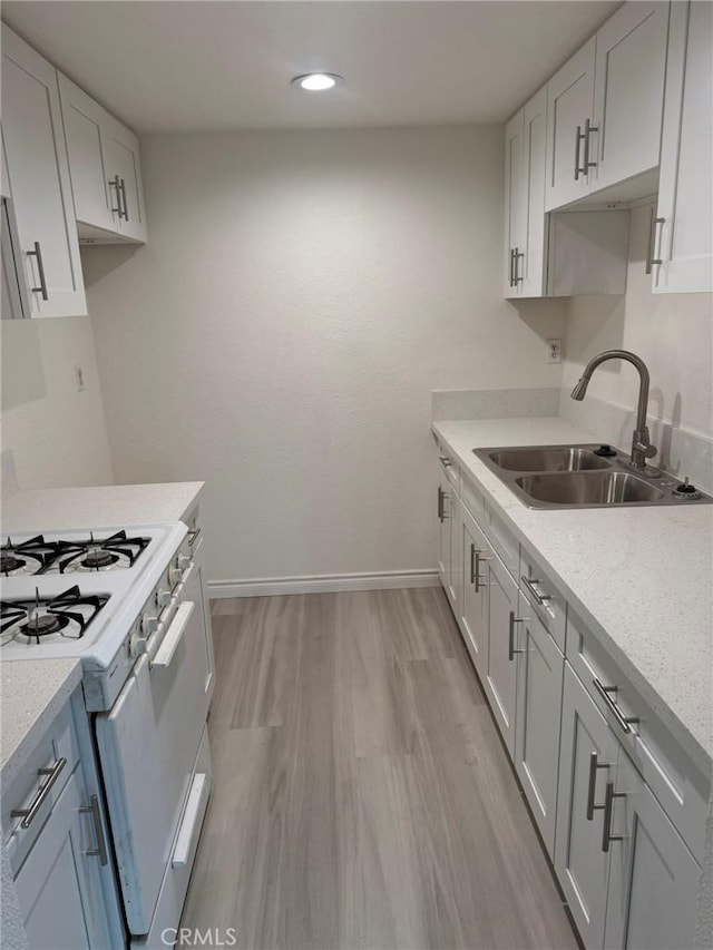 kitchen featuring recessed lighting, light wood-style flooring, a sink, white range with gas stovetop, and baseboards