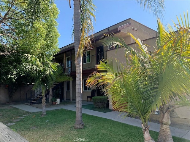 view of home's exterior featuring a balcony, stairs, a yard, stucco siding, and a patio area