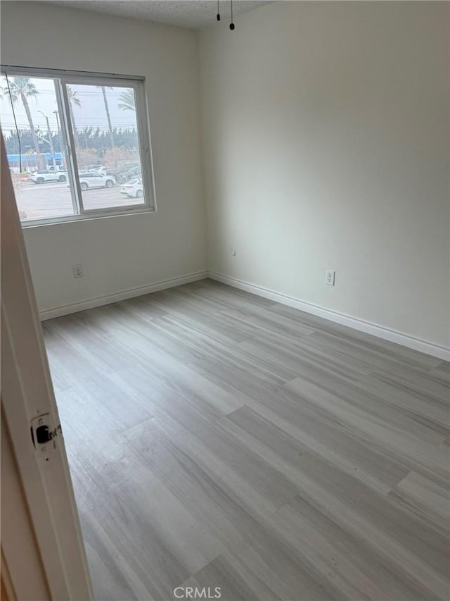 spare room featuring a textured ceiling, wood finished floors, and baseboards