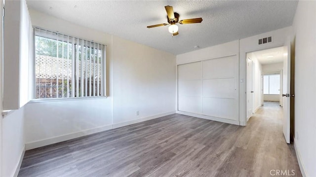 unfurnished bedroom featuring a closet, visible vents, a textured ceiling, and wood finished floors