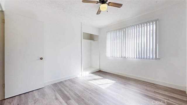 unfurnished bedroom with a closet, a textured ceiling, baseboards, and wood finished floors