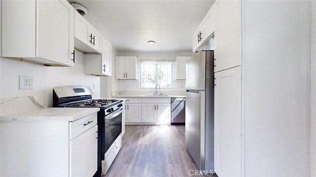 kitchen featuring light wood finished floors, white cabinets, appliances with stainless steel finishes, light stone countertops, and a sink