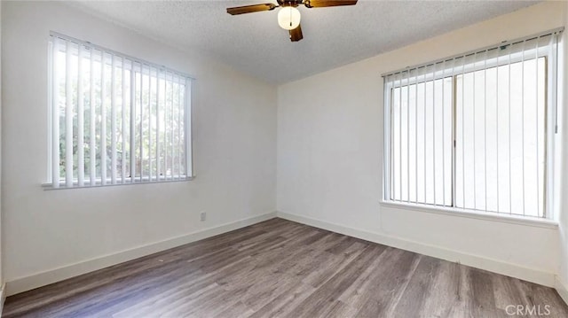 empty room featuring a textured ceiling, baseboards, and wood finished floors