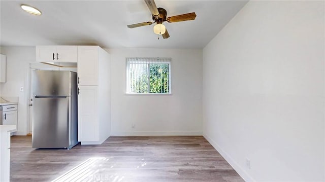 kitchen featuring light countertops, light wood-style flooring, freestanding refrigerator, white cabinetry, and baseboards