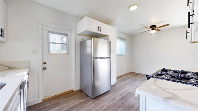 kitchen featuring ceiling fan, light wood-style flooring, white cabinets, freestanding refrigerator, and light stone countertops