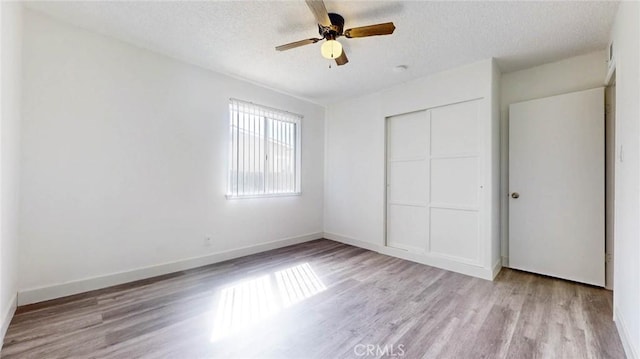 unfurnished bedroom with a textured ceiling, ceiling fan, wood finished floors, baseboards, and a closet