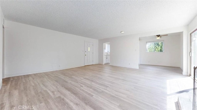 unfurnished living room featuring light wood-type flooring, ceiling fan, a textured ceiling, and baseboards