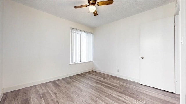 empty room featuring a textured ceiling, ceiling fan, light wood-type flooring, and baseboards