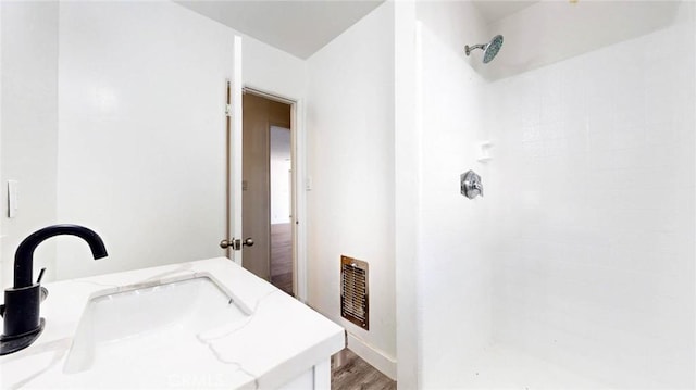 bathroom featuring visible vents, wood finished floors, a sink, and tiled shower