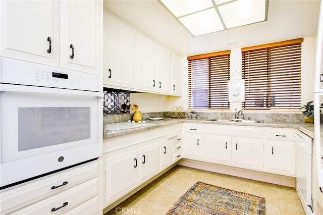 kitchen featuring light tile patterned floors, light countertops, white cabinets, a sink, and white appliances