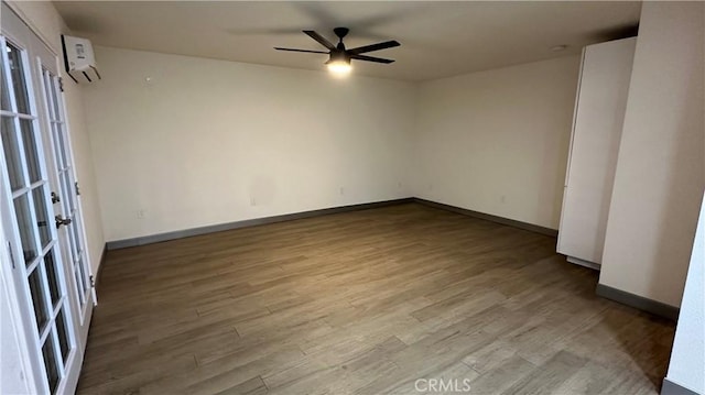 empty room with a wall mounted air conditioner, ceiling fan, baseboards, and wood finished floors