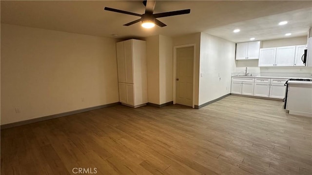 unfurnished living room with recessed lighting, a sink, a ceiling fan, baseboards, and light wood-type flooring