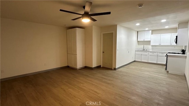 unfurnished living room with baseboards, a ceiling fan, light wood-type flooring, a sink, and recessed lighting