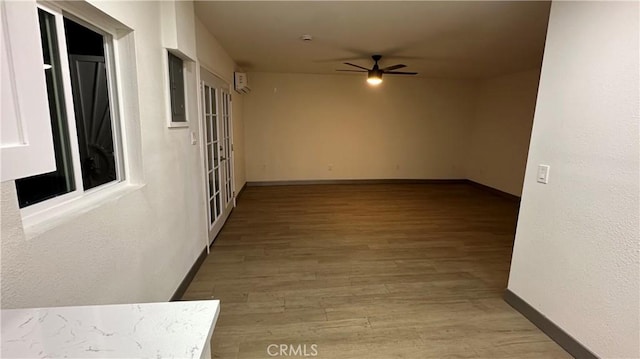 unfurnished room featuring a ceiling fan, electric panel, baseboards, and wood finished floors