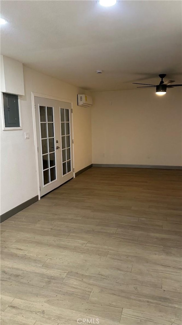 spare room with french doors, an AC wall unit, light wood-type flooring, electric panel, and baseboards