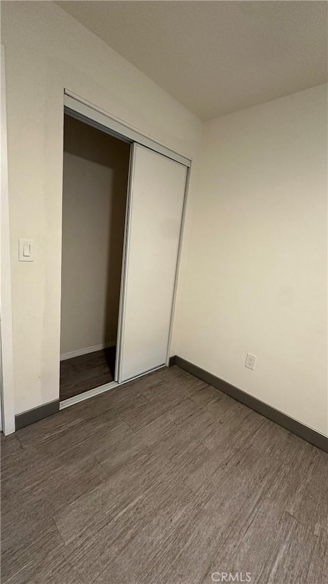 unfurnished bedroom with dark wood-type flooring, a closet, and baseboards